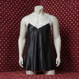 Könnte beinhalten: Ein schwarzes Satin-Slip-Kleid mit weißer Spitzenborte auf einer Schaufensterpuppe. Das Kleid hat dünne Träger und einen V-Ausschnitt. Die Schaufensterpuppe steht auf einer roten Oberfläche mit weißen Punkten.