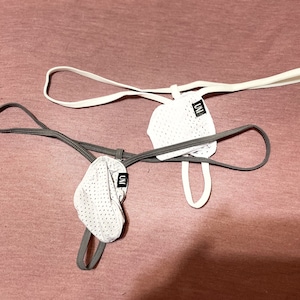 May include: Two gray and white mesh undergarments with adjustable straps. The undergarments have a small black tag with the word "UNI" printed on them.