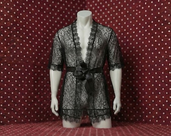 May include: Black lace robe with a matching belt and shorts, displayed on a mannequin. The robe features a floral lace pattern and scalloped edges. The mannequin is set against a red background with white polka dots.