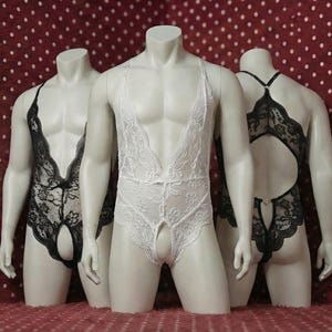 Può includere: Tre manichini espongono lingerie. Il manichino centrale indossa lingerie di pizzo bianco con scollatura profonda e cavallo aperto. I manichini laterali mostrano lingerie di pizzo nero con design simili. Lo sfondo è un tessuto rosso a pois bianchi.