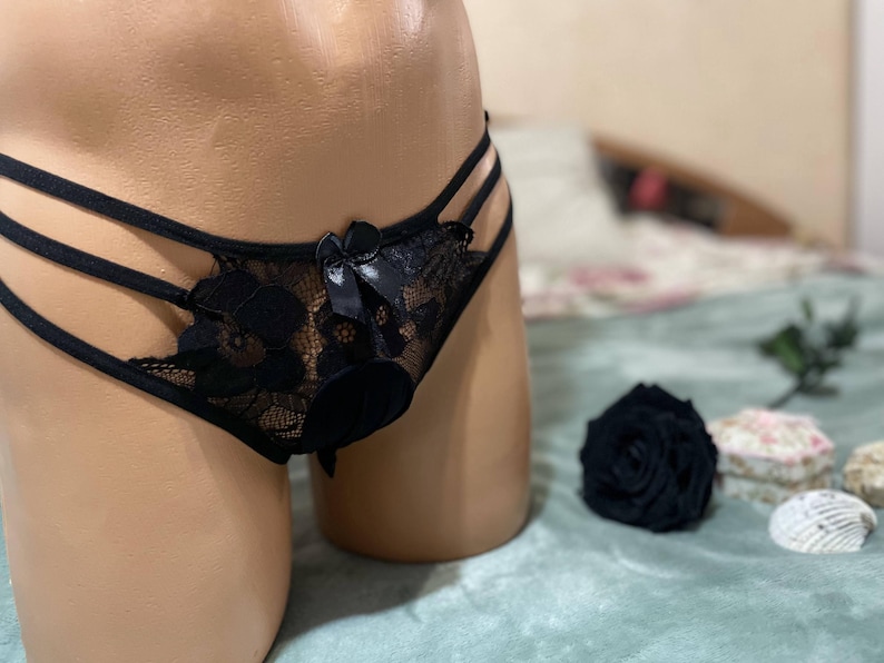 K&ouml;nnte beinhalten: Schwarze Spitzenunterw&auml;sche mit Schleifendetail und Ausschnitten. Die Unterw&auml;sche befindet sich auf einer Schaufensterpuppe und wird auf einer hellblauen Oberfl&auml;che pr&auml;sentiert.