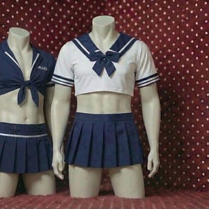 Peut inclure: Deux tenues de style marin sur des mannequins. L'une est blanche avec des détails bleu marine, un nœud et une jupe plissée. L'autre est bleu marine avec un haut noué et une jupe plissée. Les tenues sont présentées sur un fond rouge.