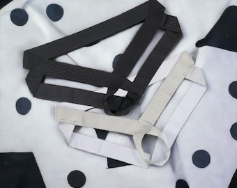 Könnte beinhalten: Zwei Ledergeschirre, eines schwarz und eines weiß, liegen auf einem weißen Stoff mit schwarzen Punkten. Die Geschirre bestehen aus Lederriemen und haben ein schlichtes Design.