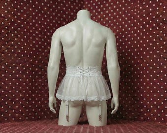May include: A white, lacy garter skirt with a corset-style back and attached garter straps. The skirt is made of sheer fabric and is displayed on a mannequin against a red background with white polka dots.