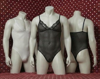 May include: Three mannequins display lingerie. The central mannequin wears a black, vertically striped bodysuit with lace trim. The other two mannequins showcase a white, vertically striped bodysuit and a black, vertically striped bodysuit.
