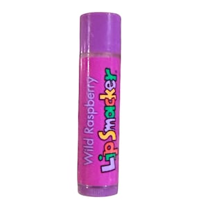 May include: A tube of Lip Smacker Wild Raspberry lip balm. The lip balm has a purple cap and a pink body with the words "Wild Raspberry" and "Lip Smacker" in a colorful font.