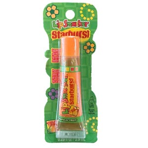 Könnte beinhalten: Lip Smacker Starburst Mango Melon Lipgloss in einer transparenten Tube mit orangefarbenem Deckel, verpackt auf einer grünen Karte mit Blumen- und Sternenmustern. Die Verpackung trägt die Aufschrift "Tropical Fruit".