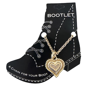 Pode incluir: Um colar com pingente em forma de coração dourado com um design detalhado, pendurado em uma corrente delicada. O pingente é exibido em um cartão preto em forma de bota, com o texto "BOOTLET" e "A CHAIN FOR YOUR BOOT".