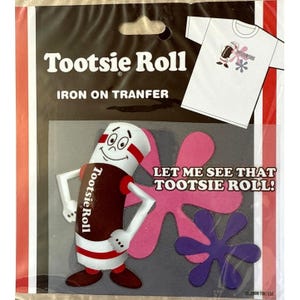 Könnte beinhalten: Eine Tootsie Roll Bügelbild-Verpackung. Die Verpackung zeigt eine Cartoon-Figur von Tootsie Roll mit einem rot-weiß gestreiften Design, die ein braunes Hemd trägt. Der Text "Tootsie Roll" und "Iron On Tranfer" sind sichtbar. Der Satz "Let me see that Tootsie Roll!" wird ebenfalls angezeigt.