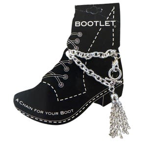 Pode incluir: Uma corrente de bota prateada com borla, exibida em um cartão preto em forma de bota. O cartão diz "BOOTLET" no topo e "A CHAIN FOR YOUR BOOT" na parte inferior. A corrente tem um fecho de alternância.