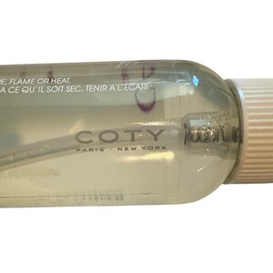 Puede incluir: Un frasco de spray Coty transparente con una tapa blanca. La botella tiene el texto "COTY PARIS NEW YORK". La botella tambi&eacute;n tiene texto en franc&eacute;s. La botella est&aacute; parcialmente llena de un l&iacute;quido transparente.