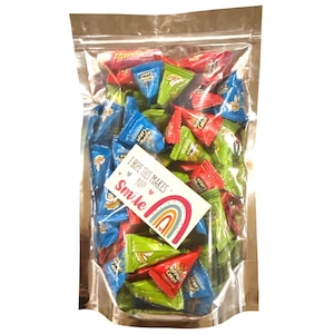 May include: A clear cellophane bag filled with colorful triangle-shaped popping candy. The candy wrappers are red, green, and blue. A small white card with a rainbow and the words "I hope this makes you smile" is inside the bag.