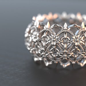 Puede incluir: Un anillo de plata con un diseño detallado e intrincado de patrones florales repetidos. El anillo es ancho y tiene una superficie texturizada.