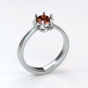 Op de afbeelding: Een zilveren ring met een rode edelsteen in een geknoopte band.