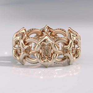 May include: A gold ring with a detailed, intricate design. The ring is made up of a series of interlocking loops and curves, creating a complex and elegant pattern.