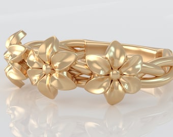 May include: A gold ring with a floral design. The ring features three stylized flowers with five petals each, intertwined with a braided band.