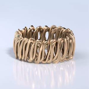 Może przedstawiać: Złoty pierścień metalowy o unikalnym, skomplikowanym wzorze z przeplatanych pętli. Pierścień jest gładki i błyszczący, z polerowanym wykończeniem.