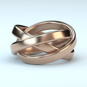 Può includere: Un anello in oro rosa con un design intrecciato unico. L'anello presenta tre fasce che si intrecciano, creando un motivo complesso e accattivante. Il metallo ha una finitura lucida, che riflette la luce. L'anello è un gioiello.