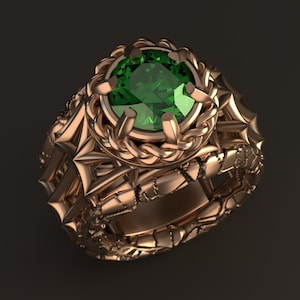 May include: A gold ring featuring a large, emerald green gemstone set within a detailed, braided design. The band of the ring is textured and has a rugged, intricate pattern.