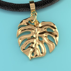 Puede incluir: Un collar de cordón negro con un colgante en forma de hoja de monstera de color dorado.