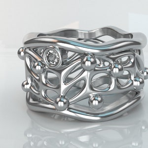 May include: A silver ring with a delicate, intricate design featuring a central diamond and multiple small spheres. The ring has a wavy, organic shape.