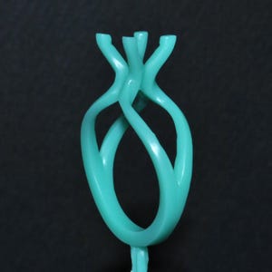 May include: A light turquoise ring casting model featuring a smooth, curved shank that splits into a four-prong setting at the top. The structure is solid and uniform in color, designed with a fluid, organic shape that tapers toward the base.