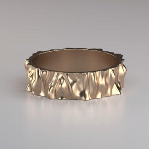 Può includere: Un anello color oro con un esterno strutturato e increspato. L'anello ha un interno liscio e un design ondulato e organico. La fascia è larga circa 1,3 cm, con un aspetto scultoreo unico.