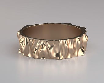Könnte beinhalten: Ein goldfarbener Ring mit einer strukturierten, gewellten Außenseite. Der Ring hat eine glatte Innenseite und ein wellenförmiges, organisches Design. Das Band ist etwa 1,3 cm breit und hat ein einzigartiges, skulpturales Aussehen.