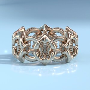 May include: A gold ring with a intricate design featuring a series of connected loops and curves. The ring is set with small diamonds.