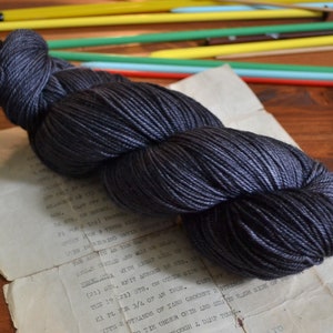 May include: A skein of dark grey yarn, wound into a loose coil. The yarn is soft and smooth, with a subtle sheen.