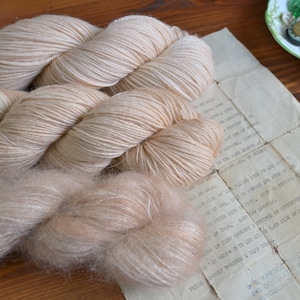 May include: Three skeins of yarn in a light beige color. The yarn is soft and fluffy, and it is perfect for knitting or crocheting.