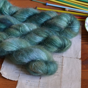 Peut inclure: Une pelote de fil bleu sarcelle et vert avec une texture duveteuse. Le fil est disposé en un tas lâche sur une surface blanche.