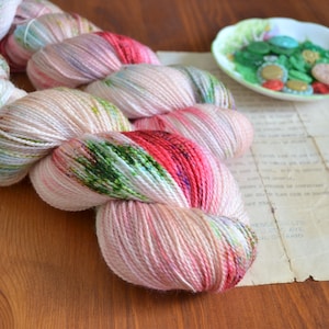 Peut inclure: Une pelote de laine rose, verte et rouge sur fond blanc. La laine est disposée en spirale lâche sur une surface en bois.