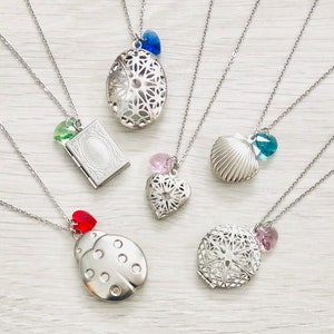 May include: Five silver locket necklaces with different charms. The charms include a seashell, a heart, a ladybug, a book, and a filigree design. Each charm has a small crystal attached to it. The crystals are blue, pink, red, green, and purple.