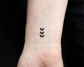 May include: A close-up of a person's wrist with a small tattoo of three black butterflies in a vertical line.