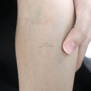Puede incluir: Un pequeño tatuaje delicado de una ola en el brazo de una persona.