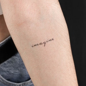 Op de afbeelding: Een close-up van iemands arm met een eenvoudige tatoeage met de tekst "imagine" in cursief schrift.