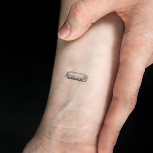 May include: A small black and white line drawing of a harmonica on a person's wrist.