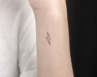 May include: A small, simple lightning bolt tattoo on a person's wrist.