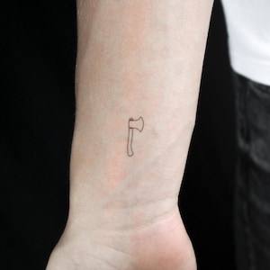 May include: A simple line drawing tattoo of an axe on a person's wrist.