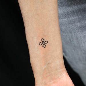 May include: A simple black geometric tattoo design on a person's wrist. The design is made up of eight squares arranged in a cross shape.