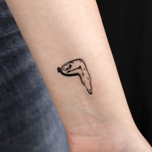 May include: A black and white tattoo of a melting clock on a person's wrist.