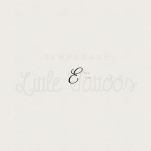 May include: A black cursive letter "E" temporary tattoo, 0.4 inches (1 cm) in height. The tattoo is displayed on a light beige background with the words "TEMPORARY" and "Little Tattoos" in a script font.