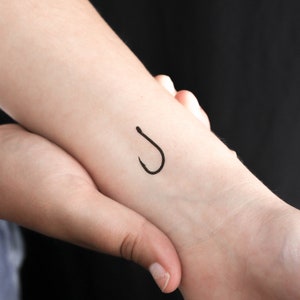 Puede incluir: Un tatuaje de un anzuelo negro en la muñeca de una persona.