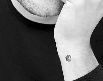 May include: A black and white outline of a seashell tattoo on a person's wrist.
