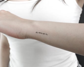 May include: A close-up of a person's arm with a small tattoo that says "amar" in cursive script.