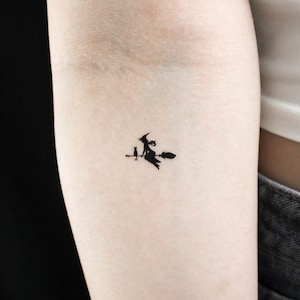 May include: A black silhouette tattoo of a witch riding a broomstick with a cat sitting on the broomstick.