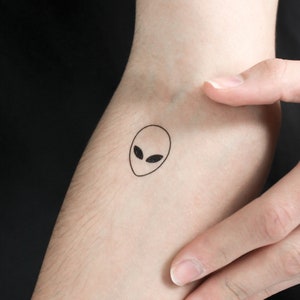 May include: A black and white temporary tattoo of an alien face.