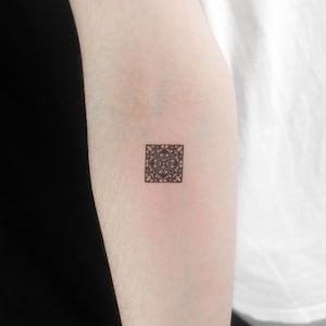 May include: A small, intricate black and white geometric design tattoo on a person's arm.