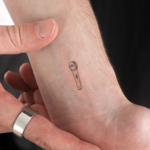 Peut inclure: Un petit dessin au trait noir et blanc d'un microphone sur le poignet d'une personne.